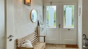 A room with a bench, a mirror, a wall-mounted light, and a door with a view of the outdoors.