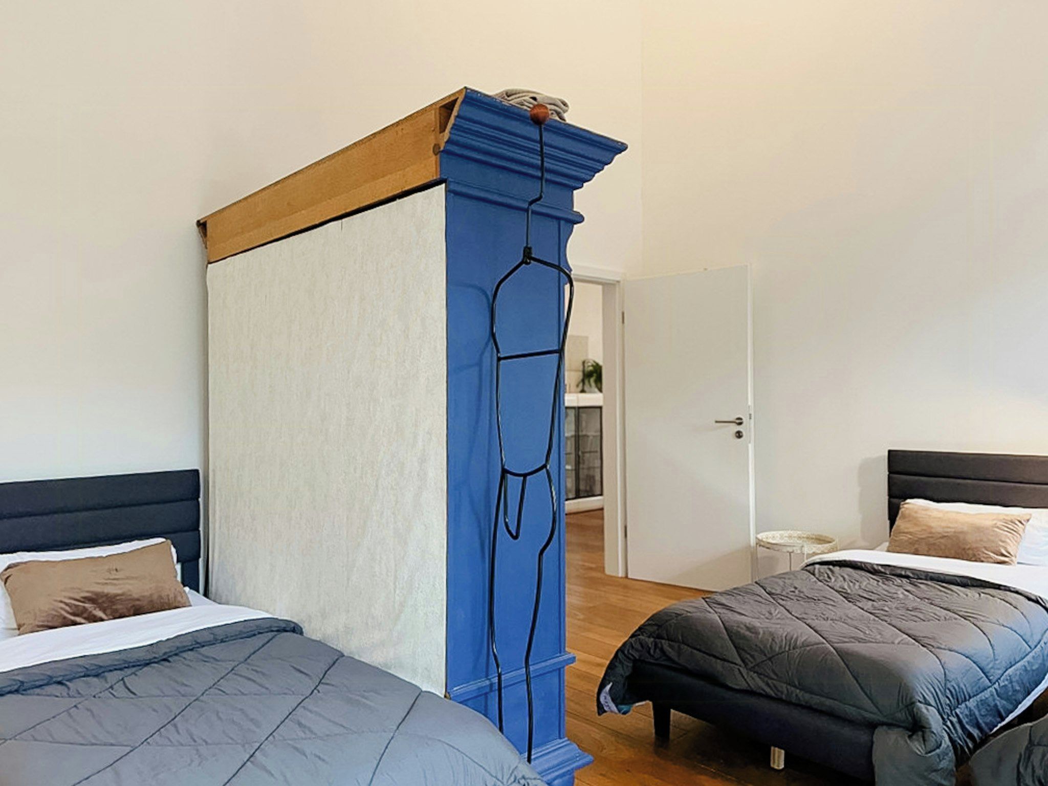 Une chambre d’hôtel avec deux lits, une cloison bleue et une tête de lit en bois.