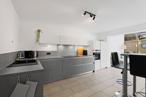 A modern kitchen with a central island, a dining area with a table and chairs, and a view of the outdoors through a window.