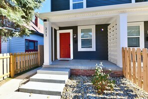 A two-story house with a red door, a front porch, and a wooden fence. - Fenced yard • pets • parking • IMS + downtown (Indianapolis)