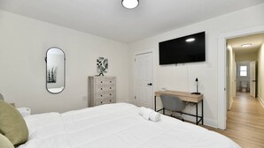 Ein Schlafzimmer mit Bett, Schreibtisch, Stuhl, Kommode, Spiegel und Fernseher.