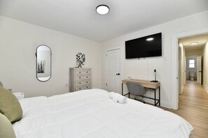 Ein Schlafzimmer mit Bett, Schreibtisch, Stuhl, Kommode, Spiegel und Fernseher.