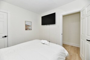 Une chambre à coucher avec un lit, un téléviseur à écran plat fixé au mur et une porte donnant sur une autre pièce.
