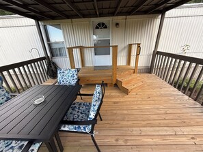 Eine überdachte Terrasse mit Holztisch und -stühlen, eine Holztreppe und eine Tür zu einem überdachten Bereich.