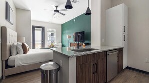 Eine moderne Küche mit einer zentralen Kochinsel, ein Essbereich mit Sofa und Tisch sowie ein Schlafzimmer mit Bett und Nachttisch.