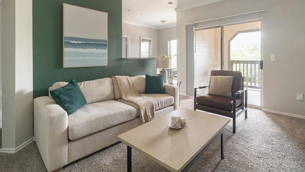 A living room with a sofa, a coffee table, and a chair. There is a painting on the wall and a window with a view. - Landing | Stylish 1BD, Gym, Clubhouse (Houston)