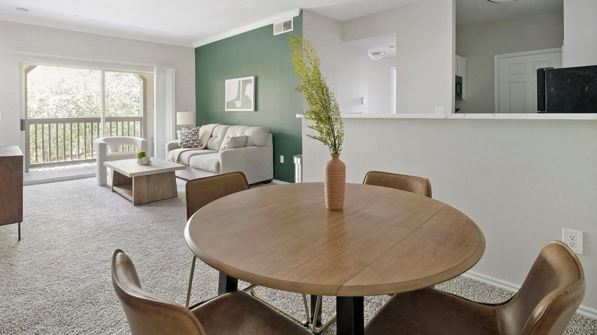 A modern living room with a round dining table, leather chairs, a sofa, and a large window.