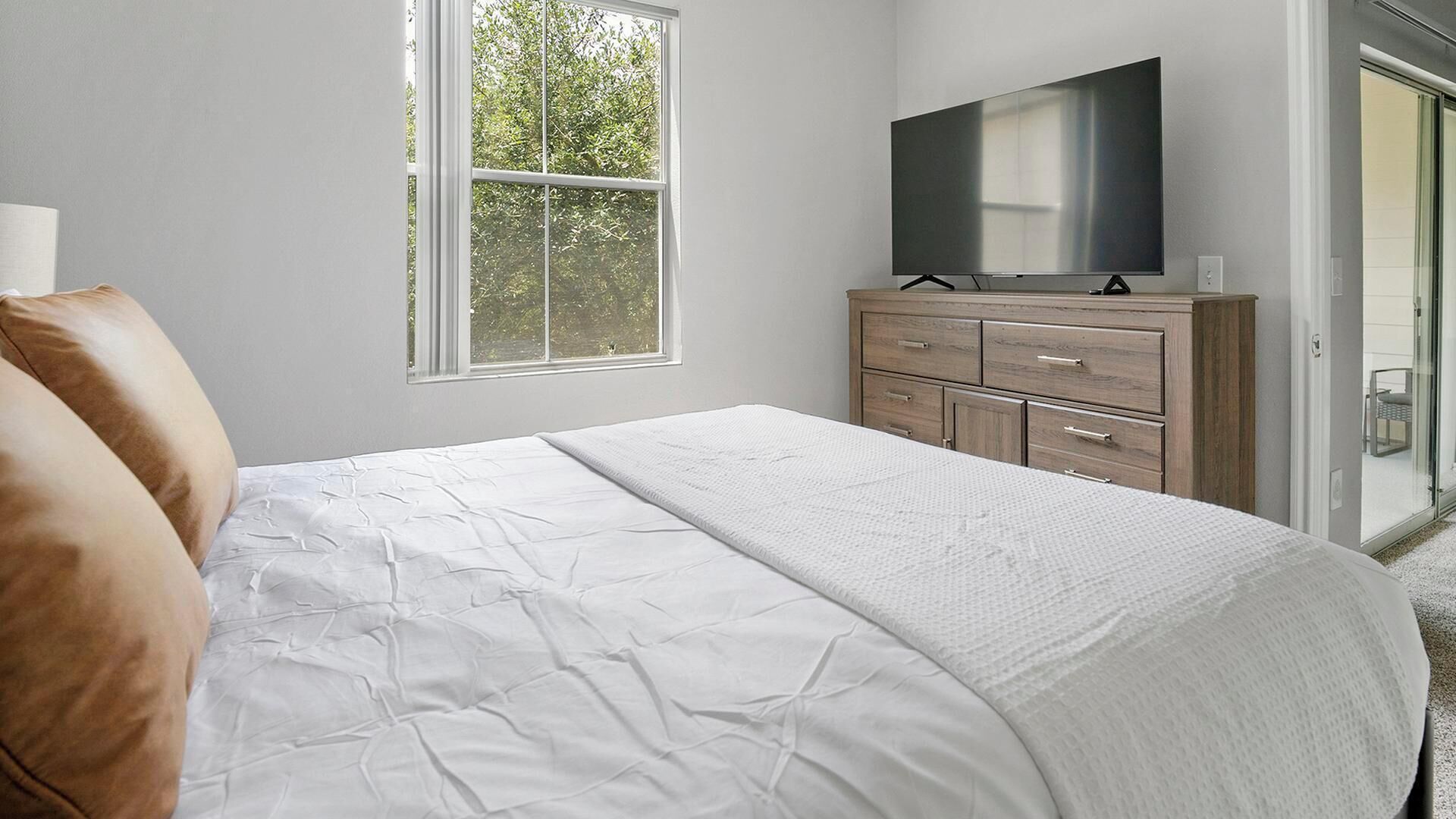 Un dormitorio con cama, televisor, cómoda y ventana.