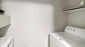 Un cuarto de lavandería con una lavadora blanca, un secador y un estante sobre el secador.
