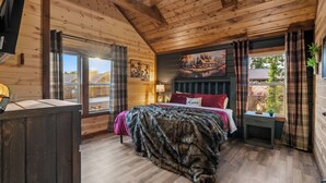 A wooden cabin bedroom with a bed, a window with curtains, a painting on the wall, and a ceiling fan. - Luxury BRAND NEW 8bdrm Cabin-Pool-Arcades-Gazebo (Sevierville)
