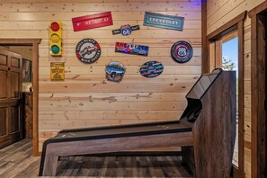 A room with wooden walls adorned with various automotive-themed stickers and signs, a bench, and a door. - Luxury BRAND NEW 8bdrm Cabin-Pool-Arcades-Gazebo (Sevierville)