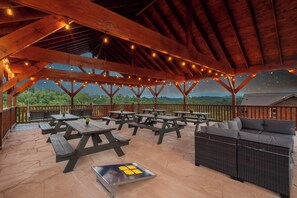 An outdoor patio with picnic tables and a sofa, under a wooden roof with string lights. - Luxury BRAND NEW 8bdrm Cabin-Pool-Arcades-Gazebo (Sevierville)