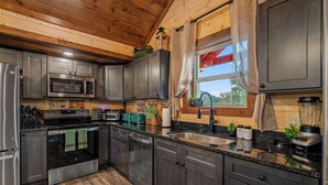 A modern kitchen with stainless steel appliances, wooden cabinets, and a granite countertop. - Luxury BRAND NEW 8bdrm Cabin-Pool-Arcades-Gazebo (Sevierville)