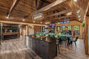 A spacious kitchen with a large island, wooden ceiling beams, and a bar area with coffee mugs. - Luxury BRAND NEW 8bdrm Cabin-Pool-Arcades-Gazebo (Sevierville)