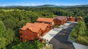 A row of log cabin-style buildings with a paved driveway and a forested backdrop. - Luxury BRAND NEW 8bdrm Cabin-Pool-Arcades-Gazebo (Sevierville)