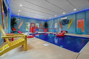 An indoor swimming pool with a blue pool floor, surrounded by colorful chairs and surfboards. - Luxury BRAND NEW 8bdrm Cabin-Pool-Arcades-Gazebo (Sevierville)