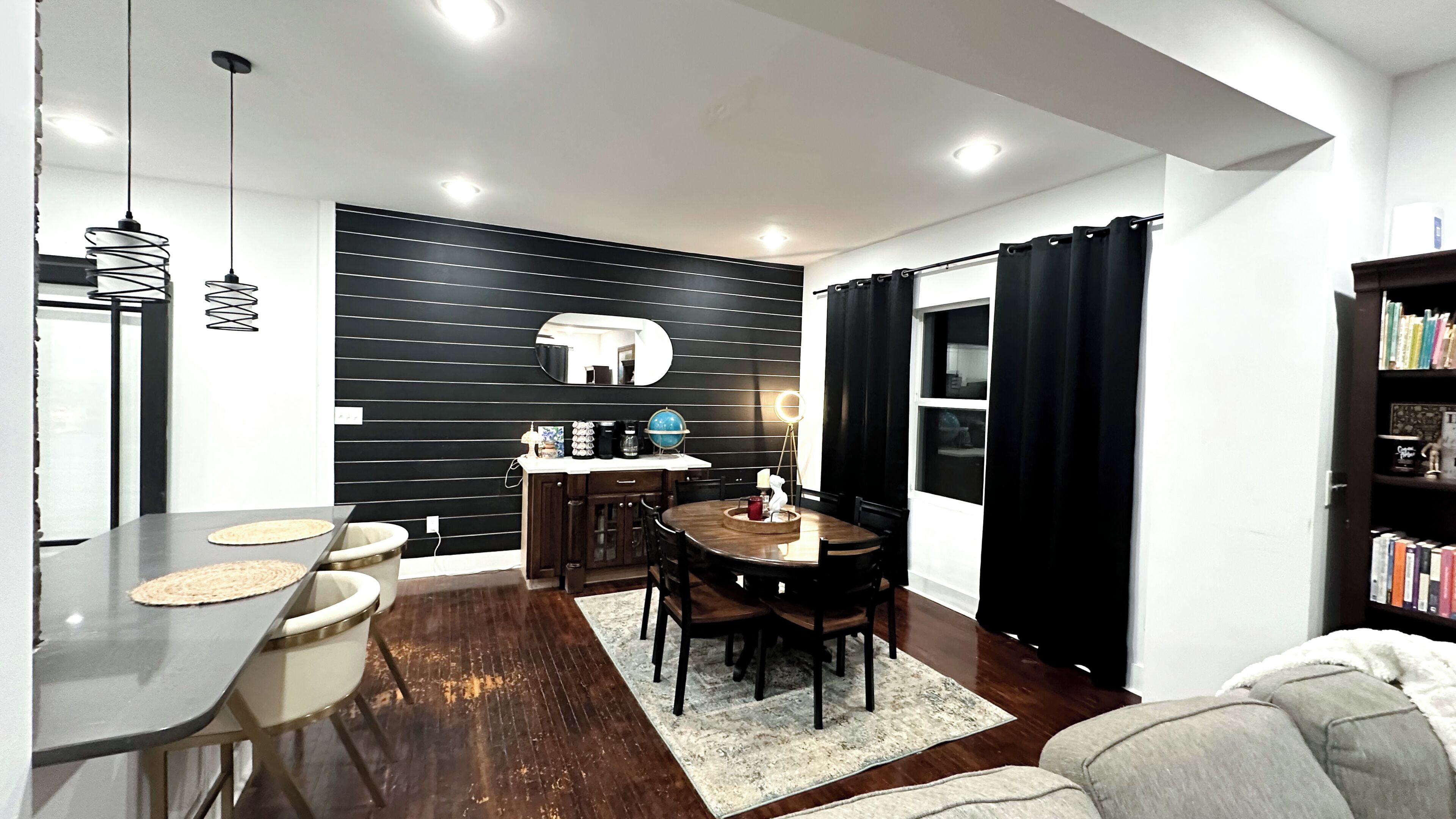 A modern dining area with a wooden table, chairs, and a black wall with horizontal lines.
