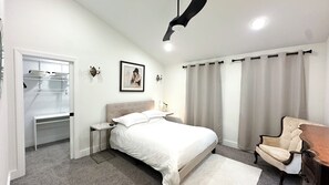 Ein Schlafzimmer mit einem Bett, einem Sessel, einem Schreibtisch, einem Kleiderschrank und einem Deckenventilator.