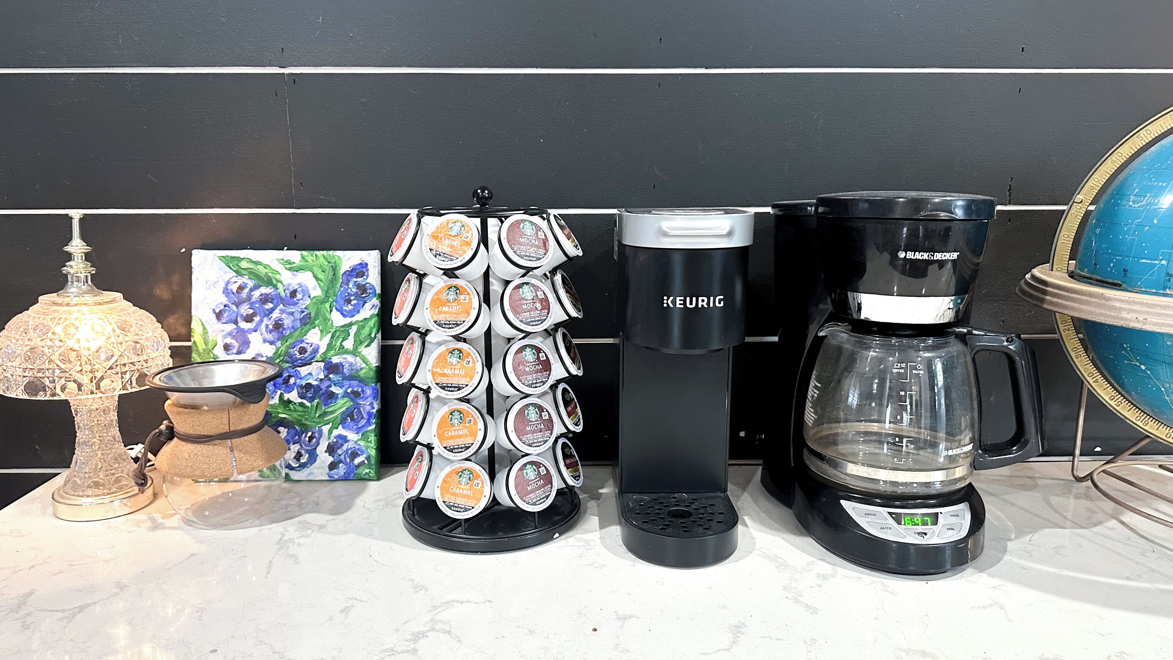 A coffee maker, a scale, a coffee grinder, and a globe on a kitchen counter.