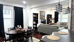 Ein Wohnzimmer mit einer Couch, einem Esstisch mit Stühlen, einem Bücherregal und einem Gemälde an der Wand.