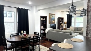 Ein Wohnzimmer mit einer Couch, einem Esstisch mit Stühlen, einem Bücherregal und einem Gemälde an der Wand.
