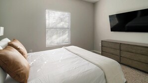 A bedroom with a bed, a dresser, a television, and a window with blinds. - Landing | Stylish 2BD, Gym, Clubhouse (Houston)