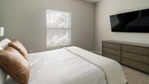 A bedroom with a bed, a dresser, a television, and a window with blinds. - Landing | Stylish 2BD, Gym, Clubhouse (Houston)
