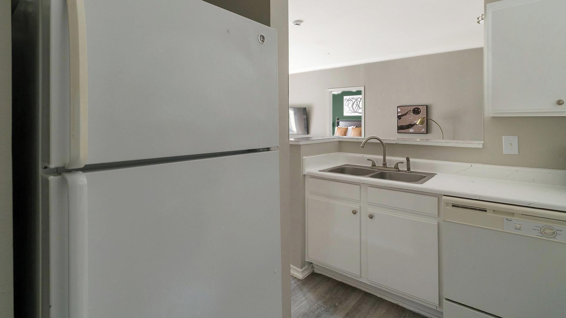 Una cocina con armarios blancos, un lavamanos doble y un refrigerador.