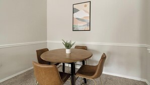 A dining area with a round table, four chairs, a potted plant, and a framed abstract artwork on the wall. - Landing | Stylish 2BD, Gym, Clubhouse (Houston)