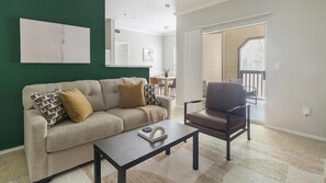 A living room with a sofa, a coffee table, and a chair. There is a dining area in the background. - Landing | Stunning 1BD, Clubhouse, Gym (Houston)