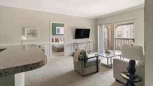 A modern living room with a flat-screen TV, a glass coffee table, a sofa, and a dining area with a round table. - Landing | Amazing 2BD, Gym, Clubhouse (Houston)