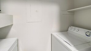 A laundry room with a white washing machine and dryer, a wall-mounted electrical outlet, and a shelf above the dryer. - Landing | Beautiful 2BD, Clubhouse, Gym (Houston)