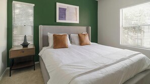 A neatly made bed with white linens and two brown pillows, a bedside table with a lamp, and a framed picture on the wall. - Landing | Beautiful 2BD, Clubhouse, Gym (Houston)
