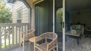 A balcony with wicker chairs and a table, a sliding glass door, and a view of greenery. - Landing | Stunning 2BD, Clubhouse, Gym (Houston)