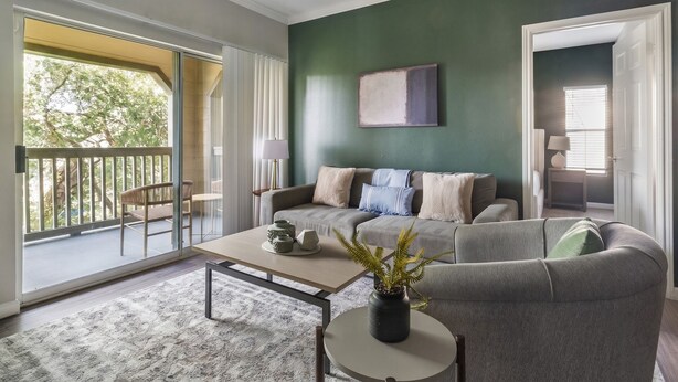 A living room with a sofa, a coffee table, and a plant. There is a sliding glass door leading to a balcony. - Landing | Amazing 2BD, Gym, Clubhouse (Houston)