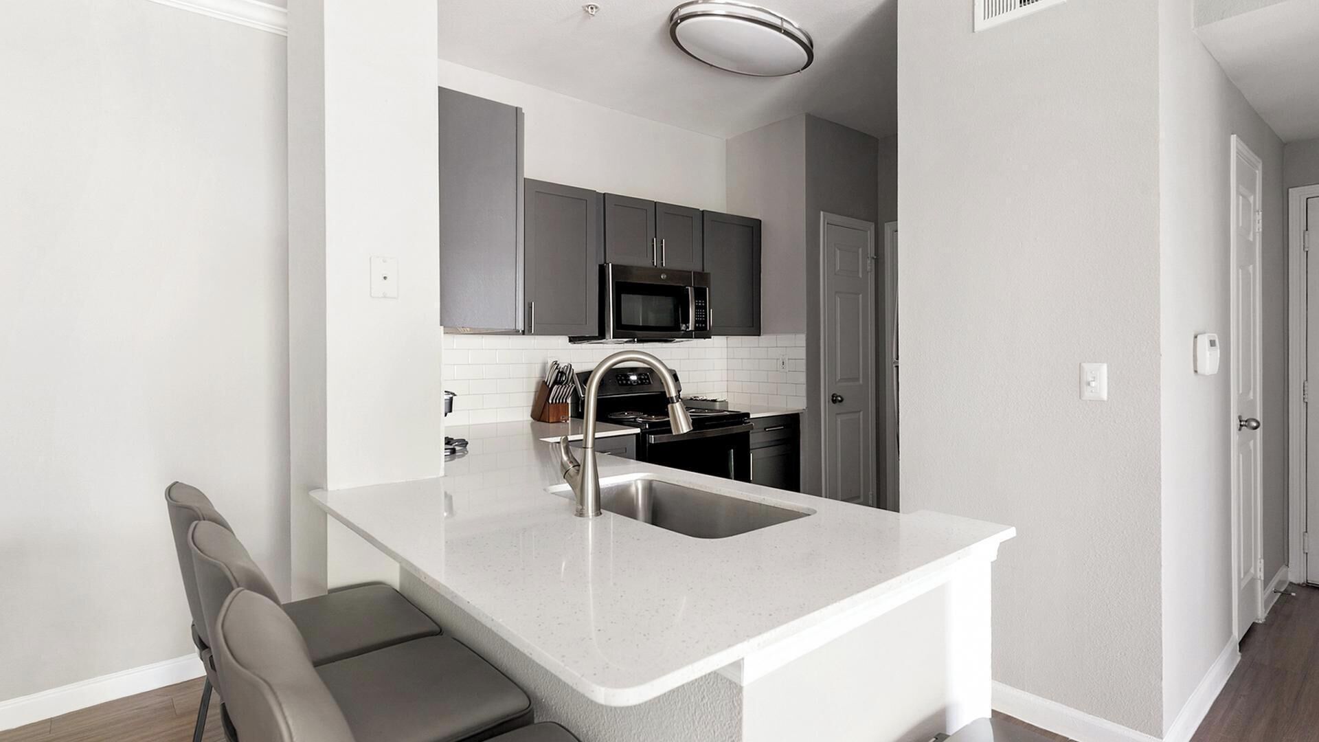 A compact kitchen with a built-in microwave, a stainless steel sink, and a grey countertop.