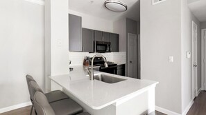 A compact kitchen with a built-in microwave, a stainless steel sink, and a grey countertop. - Landing | Stunning 2BD, Clubhouse, Gym (Houston)