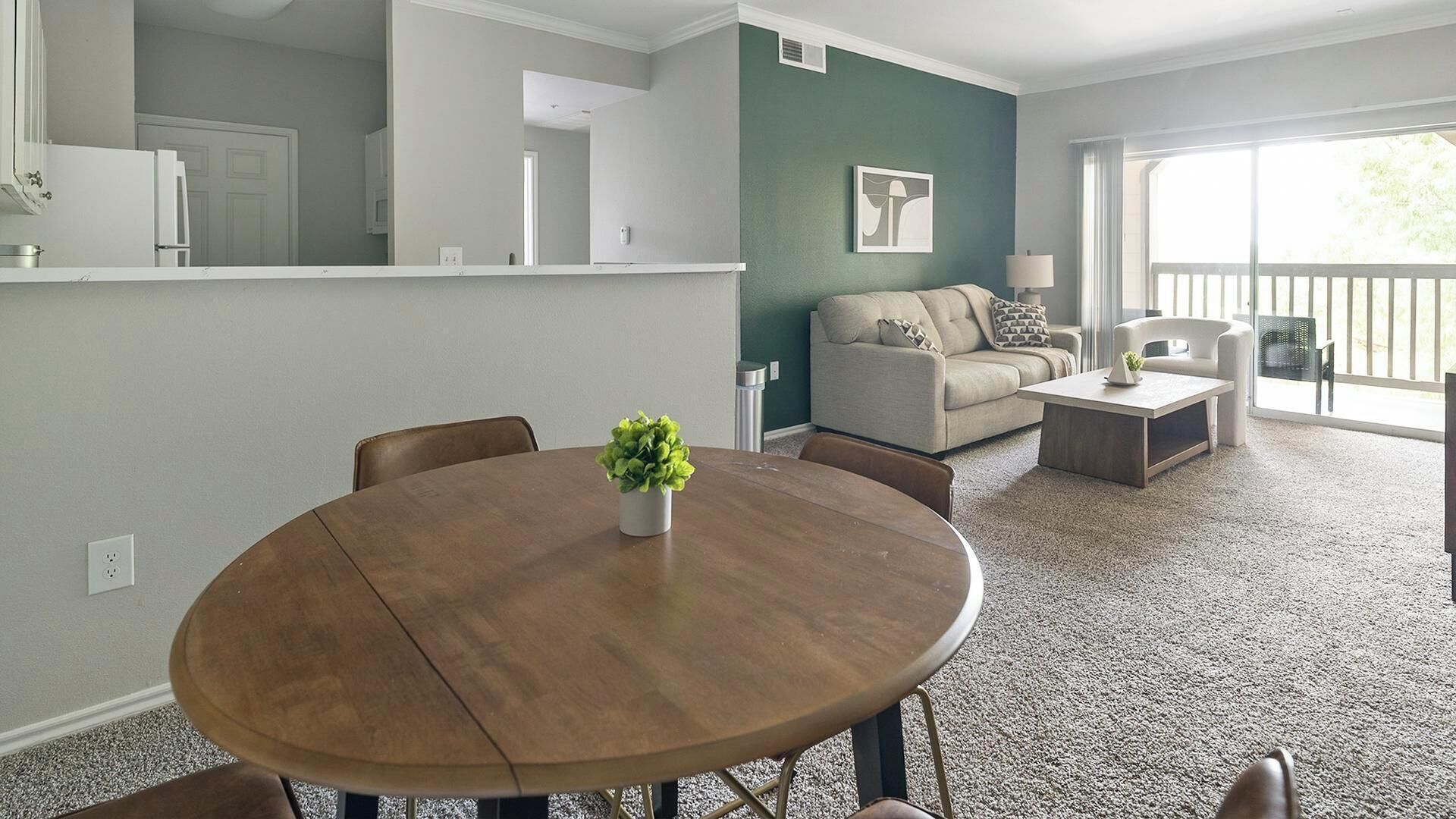 A living room with a round wooden table, a sofa, and a coffee table. There is a green wall and a window with a view.