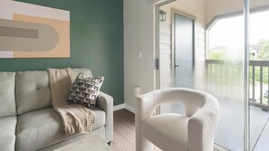 A living room with a sofa, a chair, and a glass door leading to an outdoor area. - Landing | Incredible 3BD, Gym, Clubhouse (Houston)