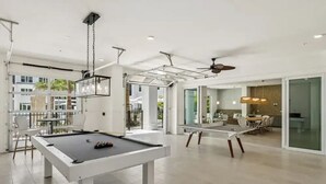 A modern indoor pool table with a dining area and a view of the outdoors. - Landing | Modern 1BD, Game Room, Gym (Punta Gorda)