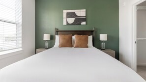 A hotel room with a bed, two bedside tables, lamps, a wall art piece, and a window with blinds. - Landing | Incredible 1BD, Yoga Studio, Game Room (Punta Gorda)