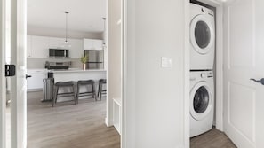 Eine moderne Küche mit weißen Schränken, einem Edelstahlkühlschrank und einer Mikrowelle. Auf der Arbeitsplatte stehen drei Barhocker und ein Blumentopf.