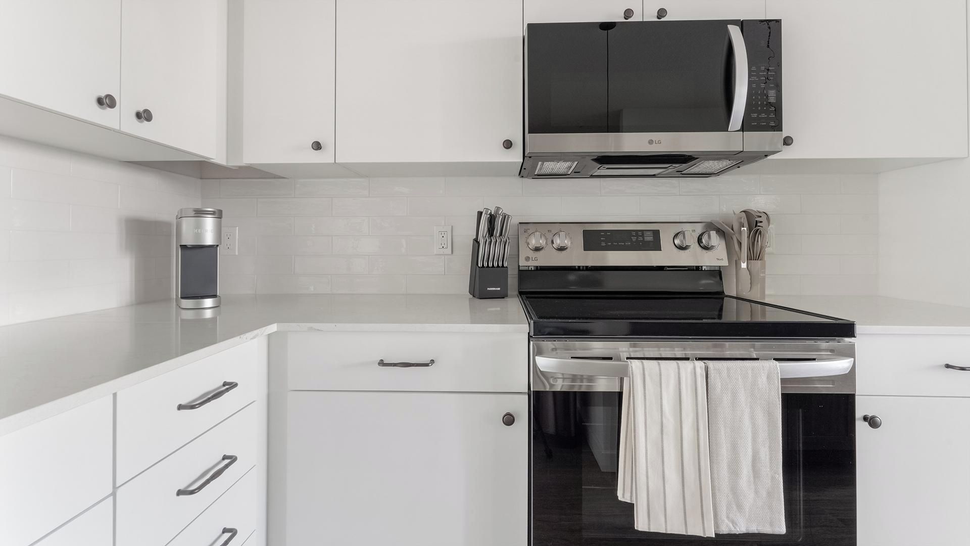 A modern kitchen with white cabinetry, a stainless steel microwave, an oven, and a coffee maker.
