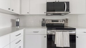 A modern kitchen with white cabinetry, a stainless steel microwave, an oven, and a coffee maker. - Landing | Modern 1BD, Game Room, Gym (Punta Gorda)