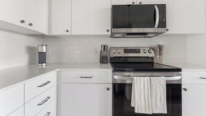 Eine moderne Küche mit weißen Schränken, einer Edelstahl-Mikrowelle, einem Backofen und einer Kaffeemaschine.