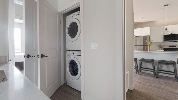 A laundry room with two washing machines, a kitchen area with a microwave and bar stools, and a wooden floor. - Landing | Spectacular 1BD, Yoga Studio, Game Room (Punta Gorda)