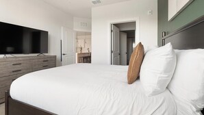 A hotel room with a bed, a television on a dresser, and a bathroom visible through an open door. - Landing | Spectacular 1BD, Yoga Studio, Game Room (Punta Gorda)