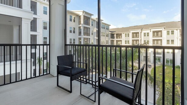 A balcony with two black chairs and a view of multi-story residential buildings. - Landing | Amazing 1BD, Gym, Game Room (Punta Gorda)