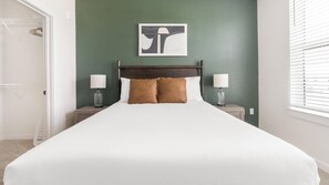 Ein ordentlich bezogenes Bett mit Kopfteil, zwei Nachttischlampen und einem an der Wand hängenden Kunstwerk.