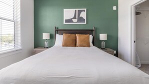 A hotel room with a large bed, two bedside lamps, a wall-mounted artwork, and a view through a window. - Landing | Stunning 1BD, Yoga Studio, Gym (Punta Gorda)